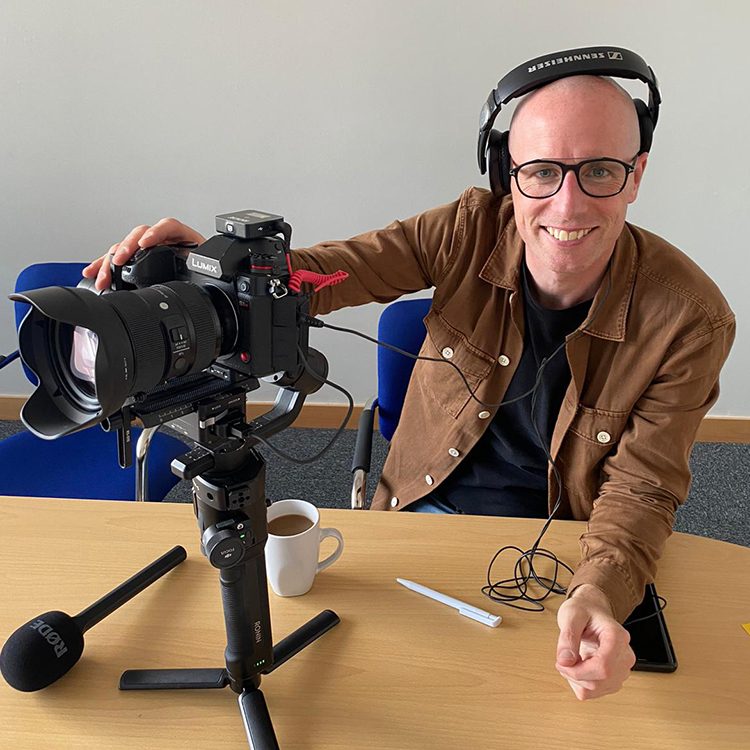 Matt Bell sits at a table with a camera and professional audio set up in Kirkby, Liverpool.