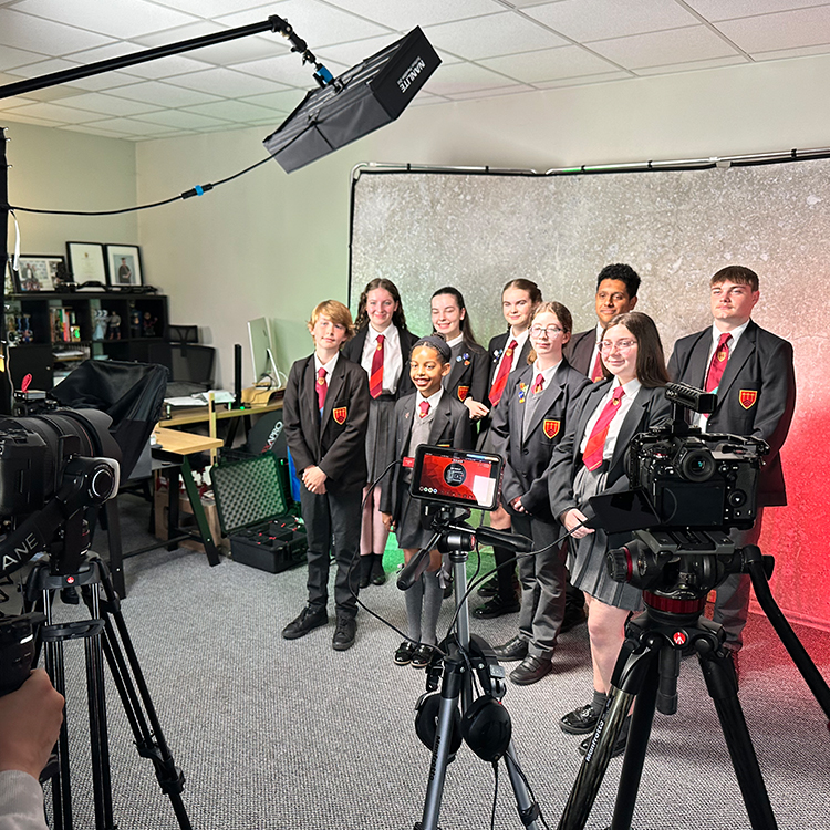 A group of school students stand in front of the cameras for a scene from a video for the school website.