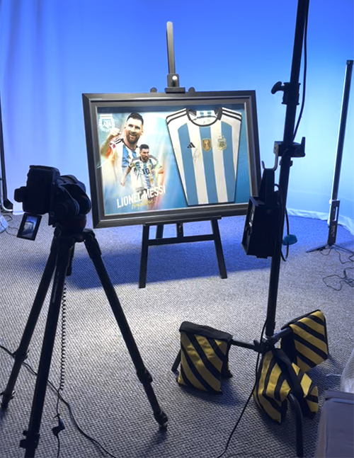 A framed signed Lionel Messi shirt stands on an easel for a creative content shoot.