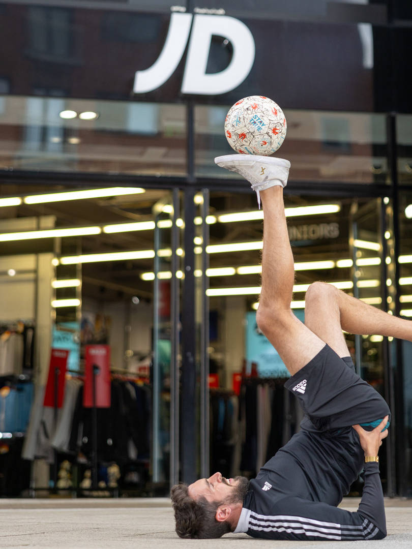 A footballer balances a football on the sole of his foot outside a JD Sports store in Wrexham.