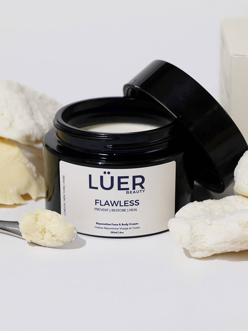 An open jar of body cream photographed on a white backdrop amongst a selection of ingredients